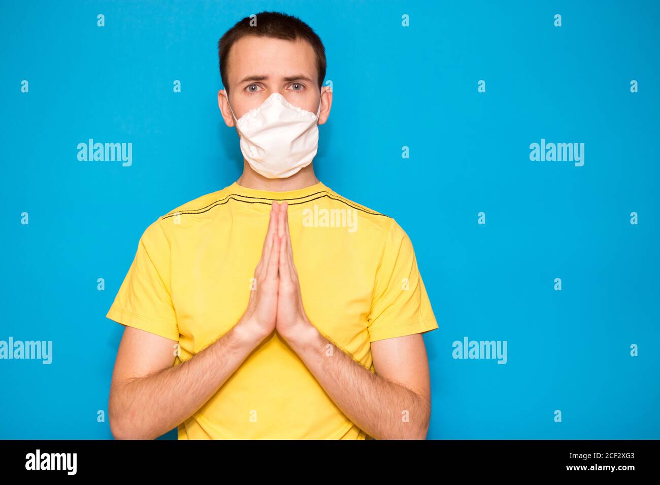 Retrato de un joven en una camiseta amarilla con máscara protectora contra el coronavirus, haciendo un gesto de rezo por la salud contra el virus de la corona es muy rápido Foto de stock