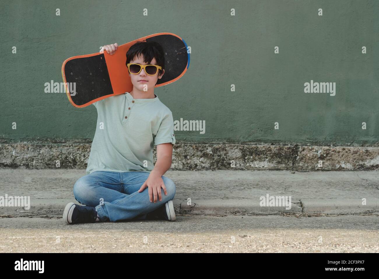niño feliz con monopatín y gafas de sol sentados en la calle Foto de stock