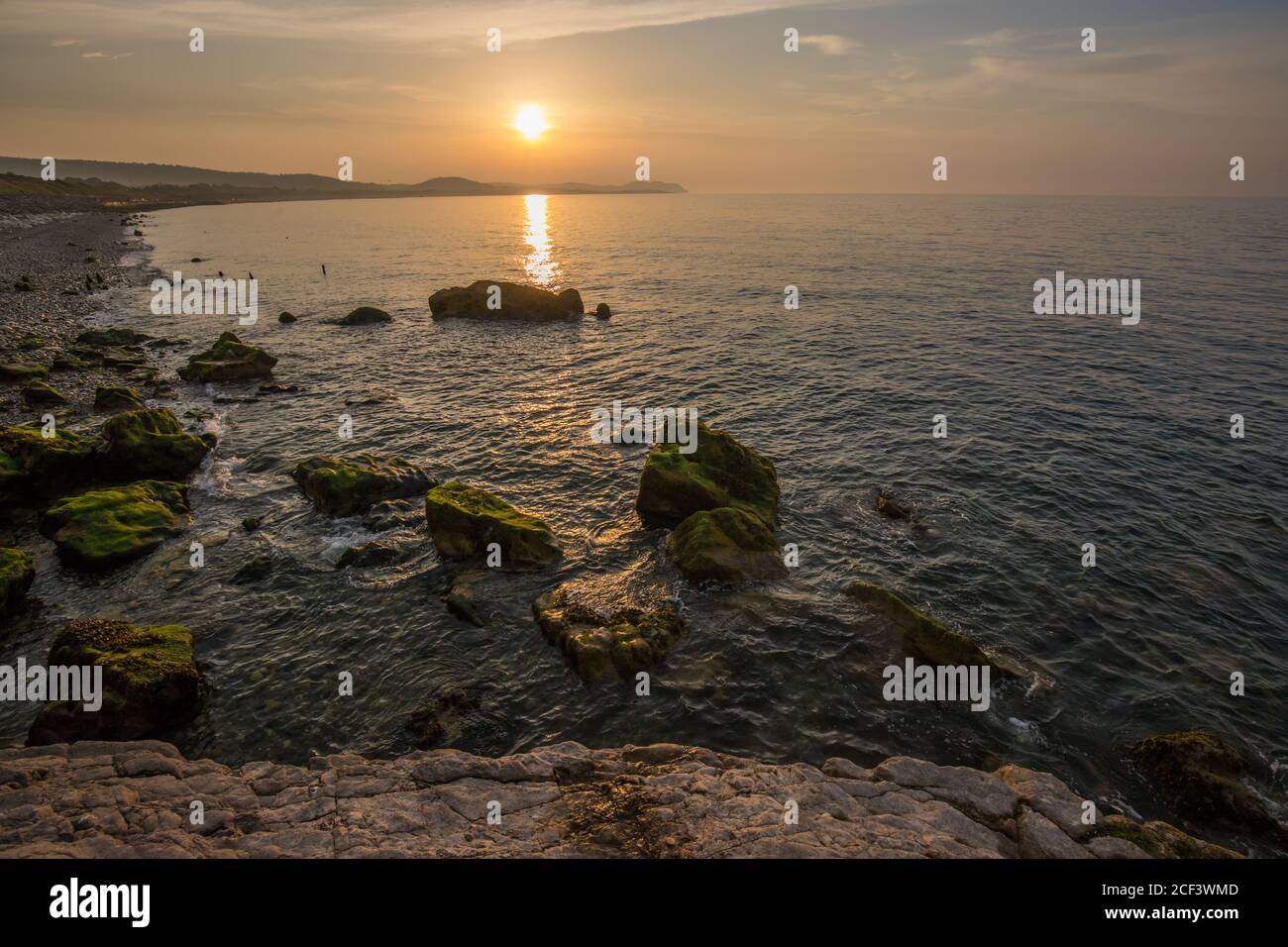 Puesta de sol de hora dorada en la bahía de Colwyn, Gales del Norte. Cielo cálido y olas suaves a lo largo de una costa rocosa Foto de stock