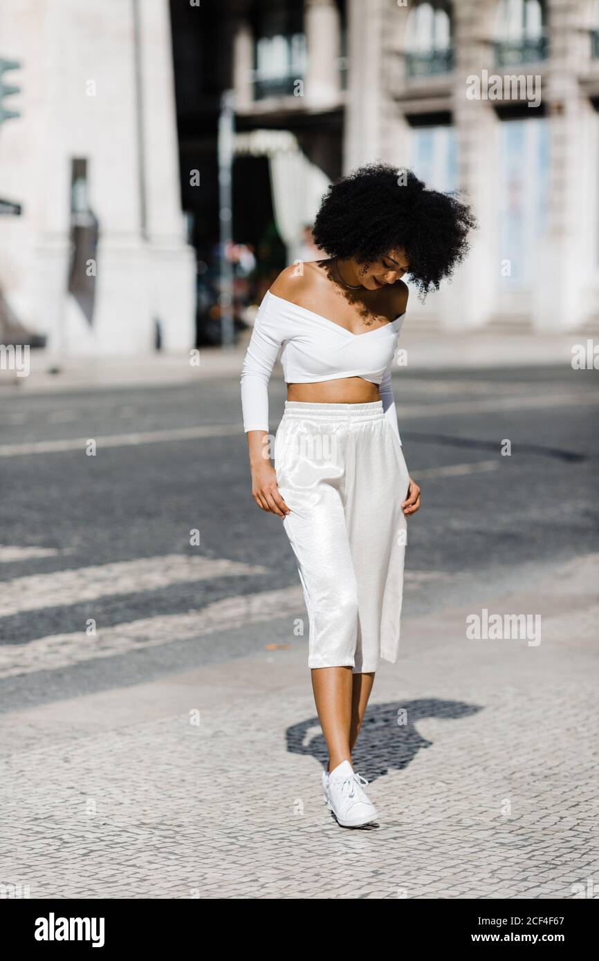 Hermosa mujer afroamericana en blanco ropa de moda de pie en la carretera  contra el fondo urbano Fotografía de stock - Alamy