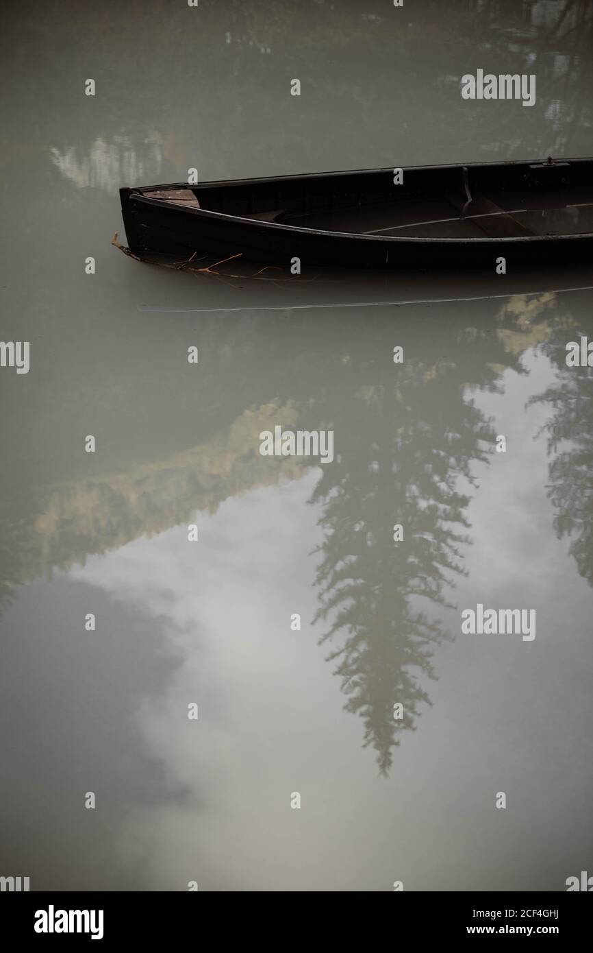 Desde arriba de agua nebulosa de lago con barco de madera Y el reflejo de los pinos y el cielo en las montañas Dolomitas Foto de stock