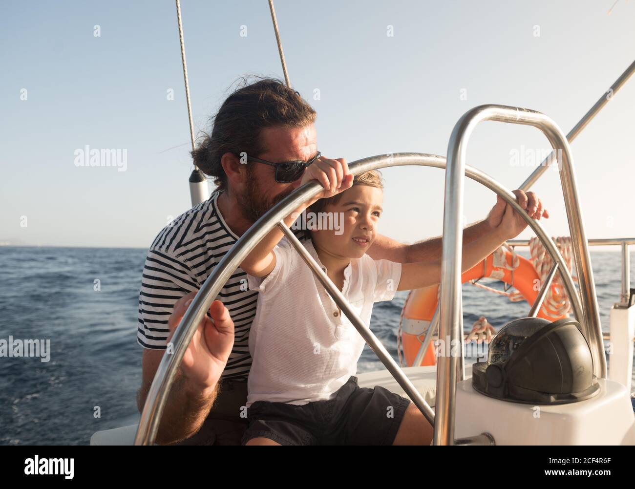 Padre e hijo flotando en barco caro en el mar y.. cielo azul en el día soleado Foto de stock