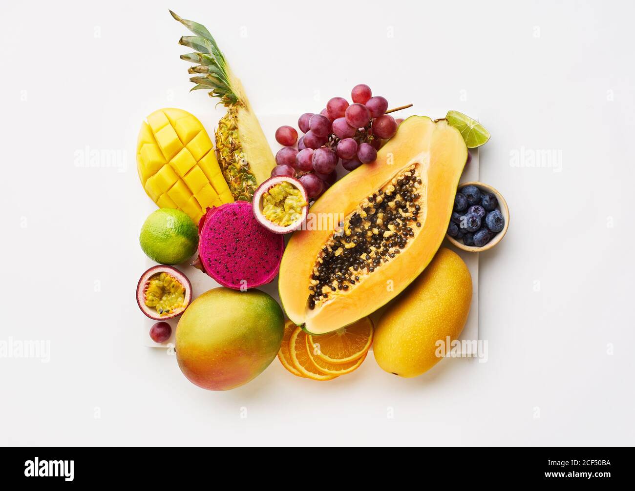 Vista superior de plano con frutas tropicales en una bandeja: Papaya, mango, fruta de dragón y piña sobre fondo blanco. Lujo de verano Foto de stock