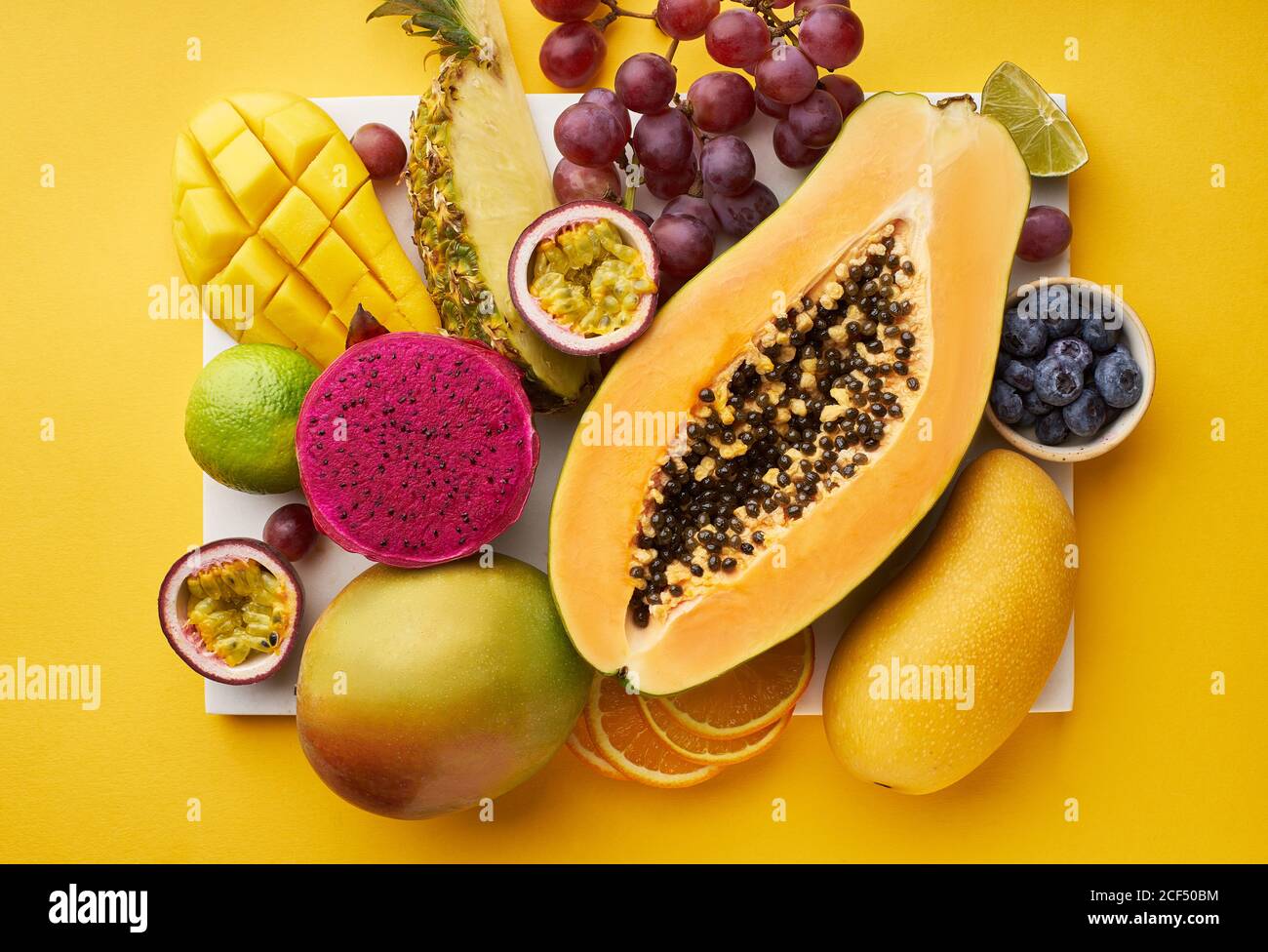 Vista superior de plano con frutas tropicales en una bandeja: Papaya, mango, fruta de dragón y piña sobre fondo amarillo. Lujo de verano Foto de stock