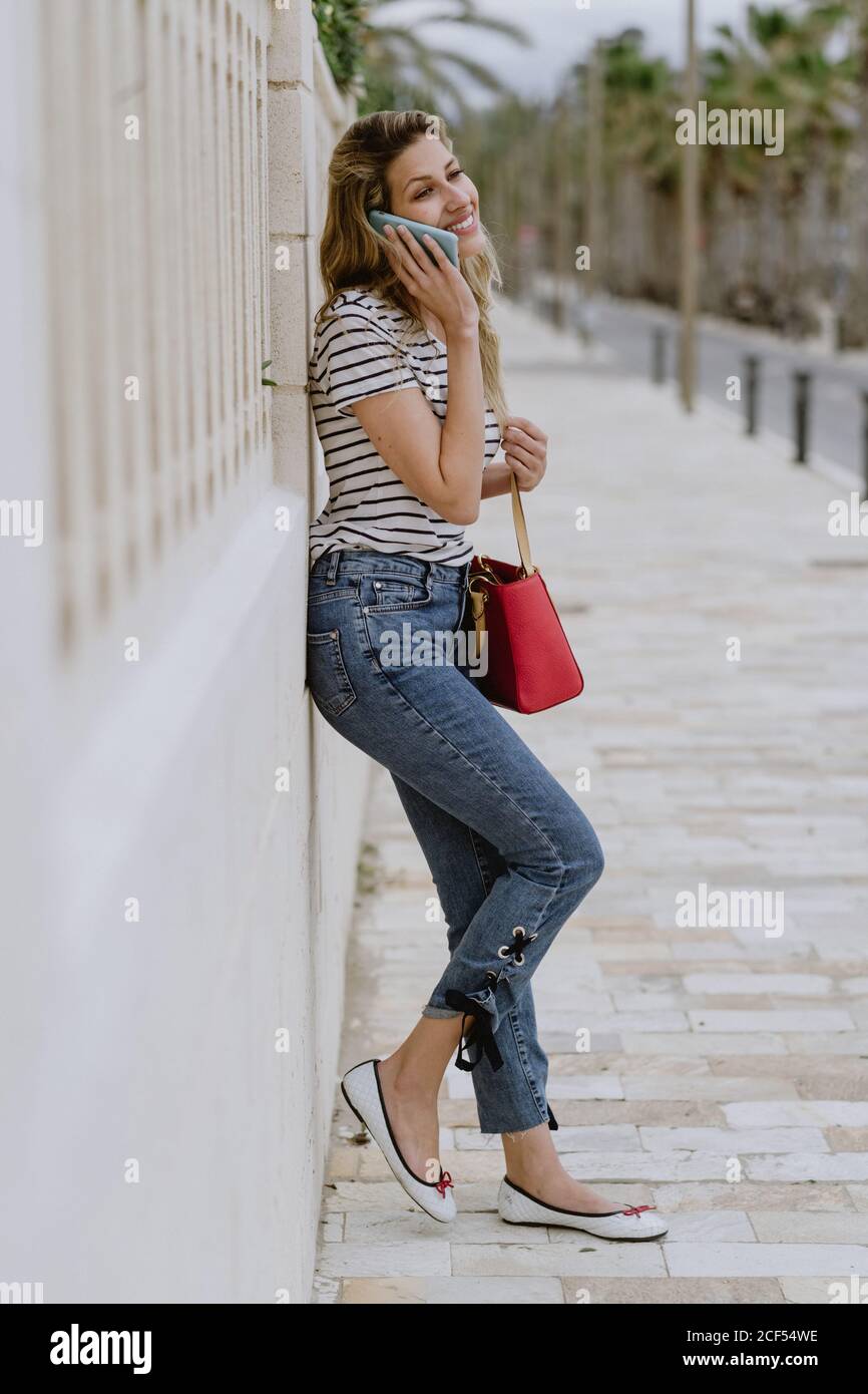 Feliz mujer joven alegre en camisa informal de rayas y jeans está al lado  del edificio en la calle de la ciudad y habla smartphone Fotografía de  stock - Alamy