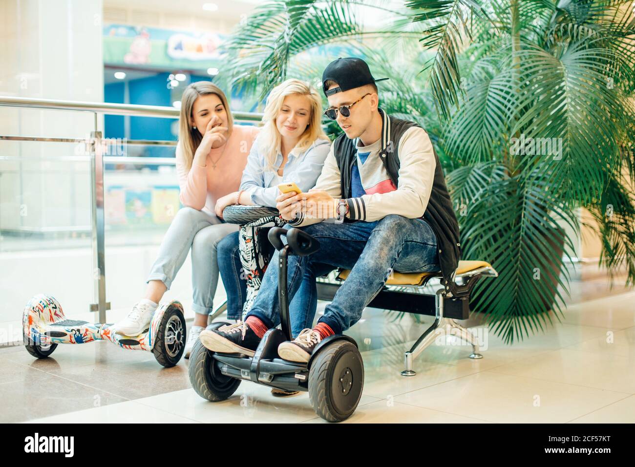 Grupo de personas modernas con scooter eléctrico hoverboard sentado en un  banco y utilizando el teléfono Fotografía de stock - Alamy