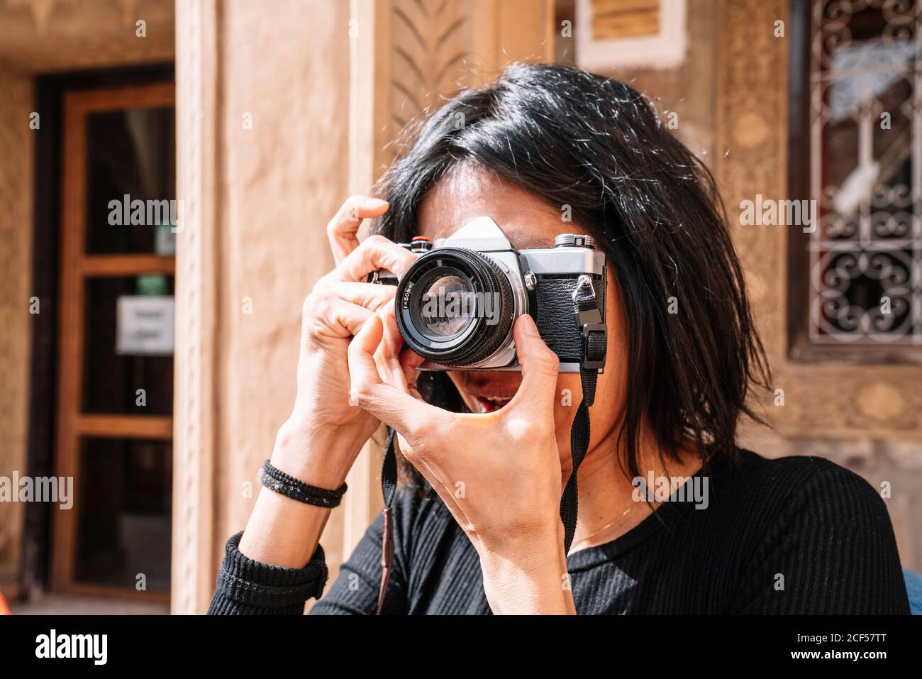 Mujer positiva con ropa informal con cámara óptica de ajuste para la sesión  fotográfica mientras está de pie fuera de la cafetería Fotografía de stock  - Alamy