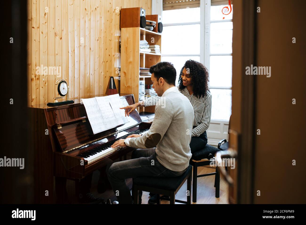 Joven aprendiendo a tocar el piano cerca de la profesora de la mujer negra en estudio de música Foto de stock