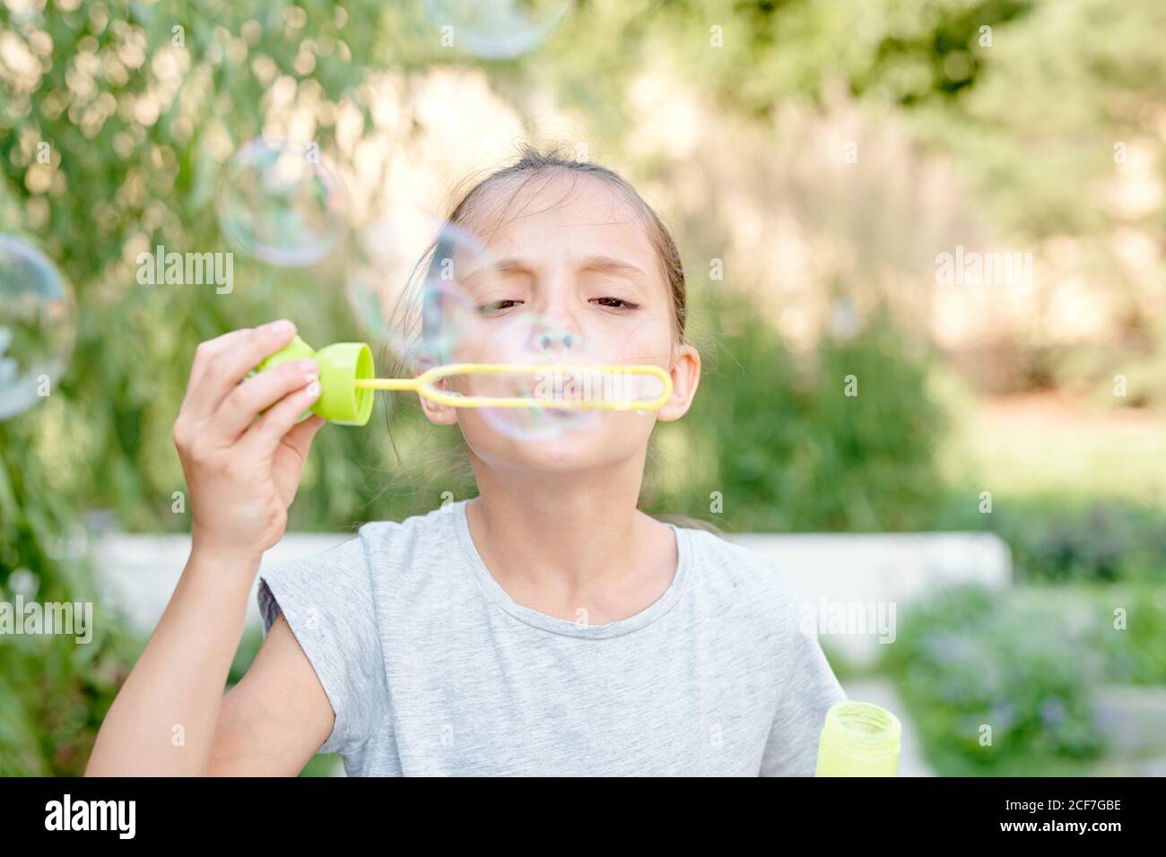 Retrato medio de cerca de una niña que se divierte inflando burbujas de jabón el día de verano Foto de stock