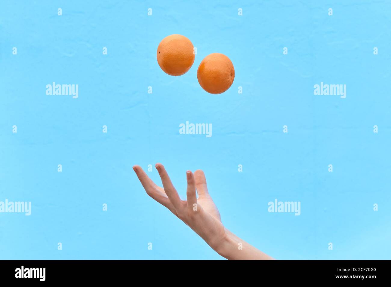 La mujer de la cosecha lanza naranja fresca en el aire mostrando el concepto de dieta saludable sobre fondo azul Foto de stock