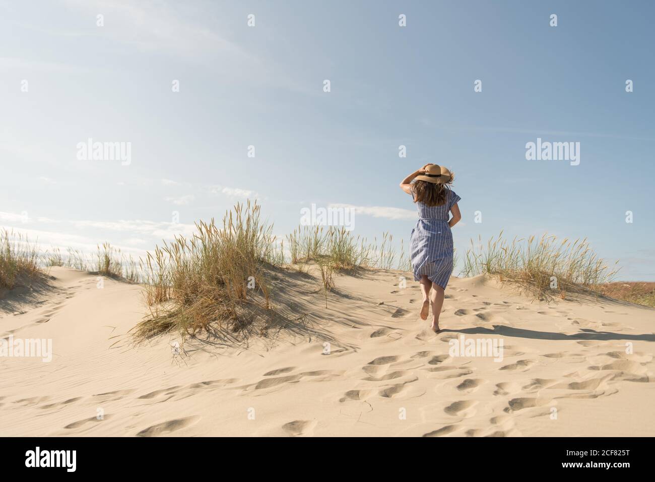 mujer adulta en vestido casual y sombrero de paja caminando teniendo buen tiempo en la duna de arena en el día caluroso de verano Foto de stock