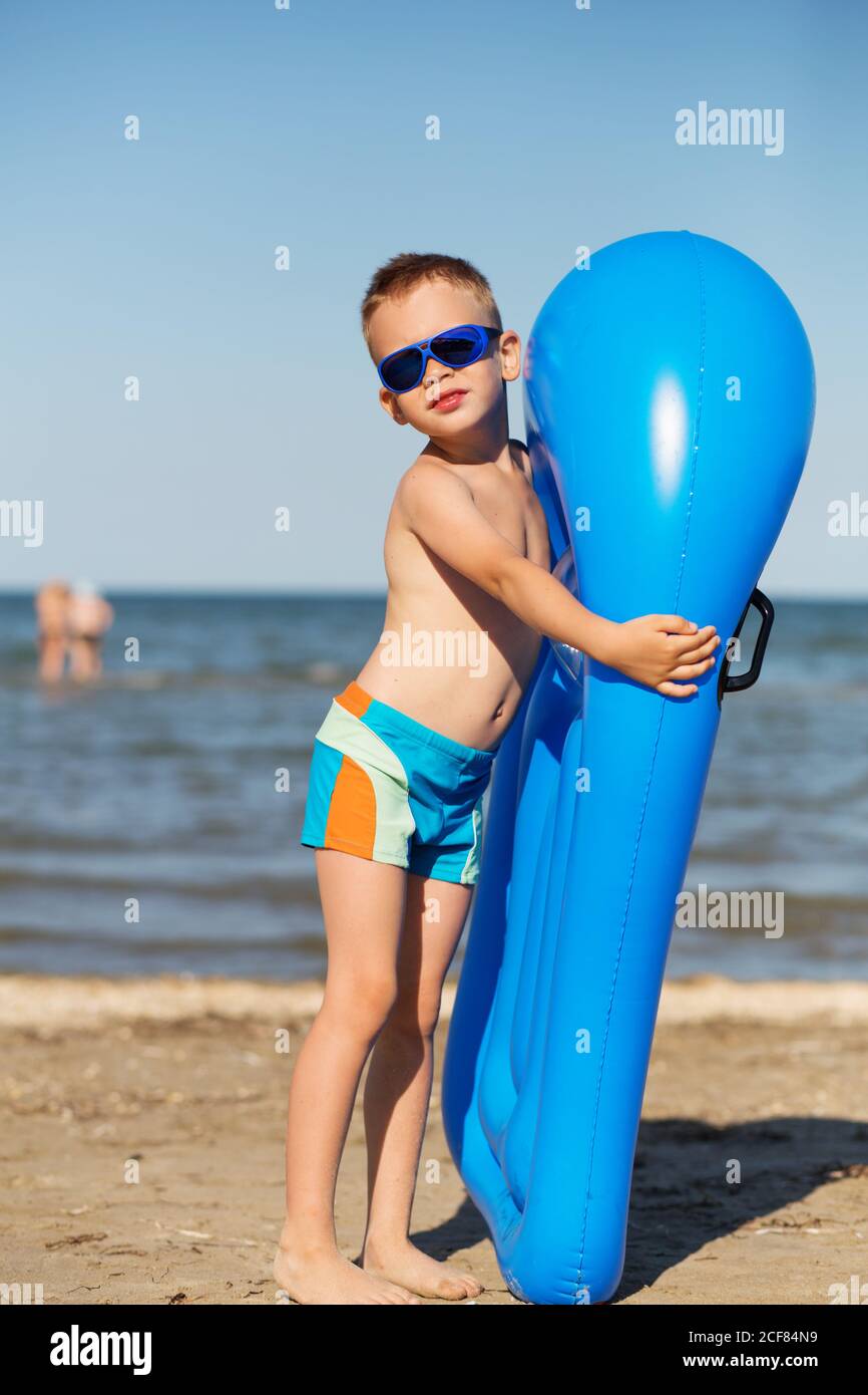 Niño pequeño sosteniendo un colchón inflable en la playa el día caluroso de  verano. Niño sonriente jugando en la playa con colchón de aire. El niño va  a nadar Fotografía de stock -
