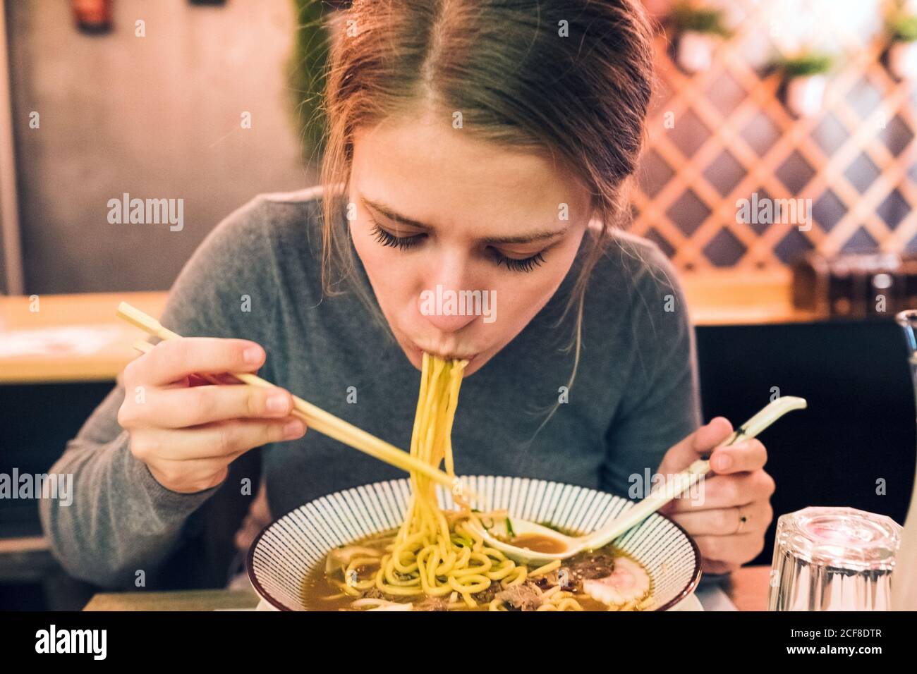Mujer joven usando palillos y cuchara para comer ramen sabroso Mientras  estaba sentado en una mesa en un restaurante japonés Fotografía de stock -  Alamy