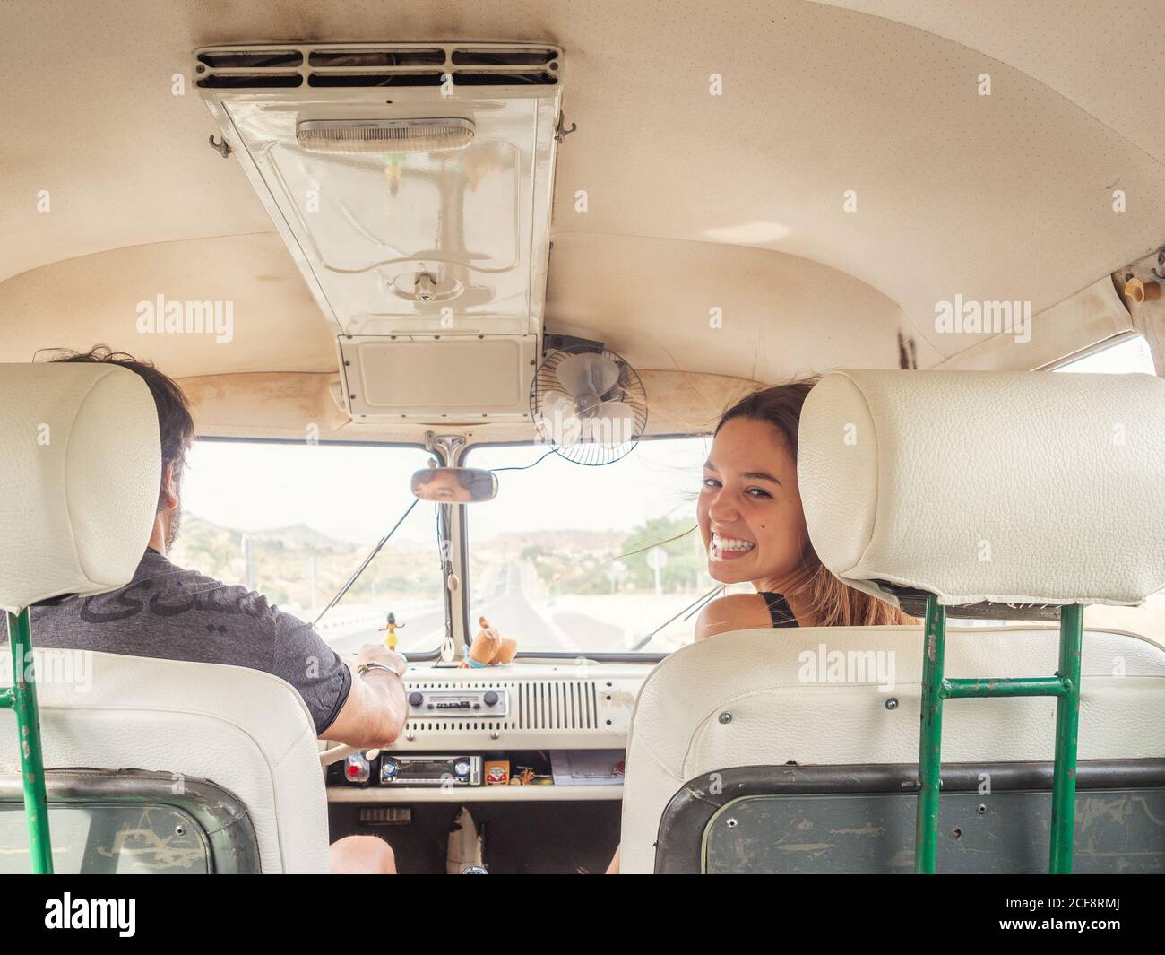 Vista posterior de hombre irreconocible conductor y joven mujer sonriente sentado frente al coche mirando la cámara Foto de stock