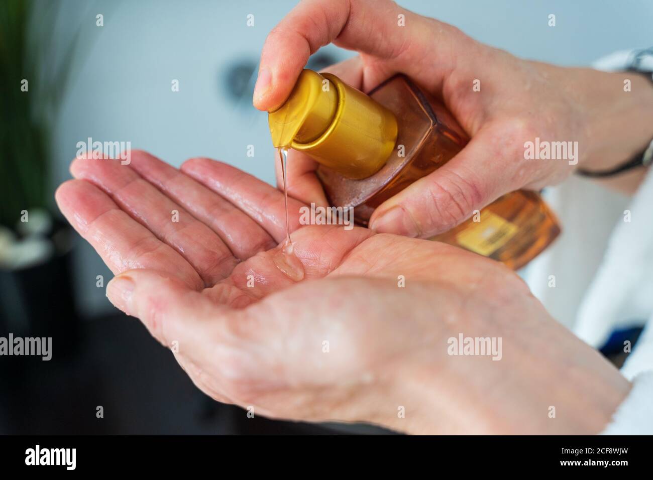 Cosecha hembra adulta de pie en el cuarto de baño con botella de plástico y. uso de líquido para el cabello en la mano para el tratamiento del cabello Foto de stock