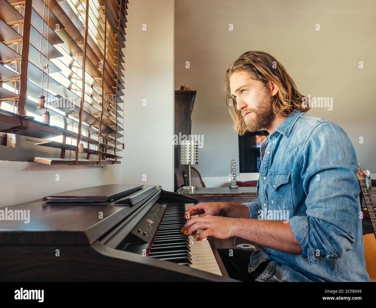 Hombre brutal y pensivo que compone la melodía en el piano electrónico en el apartamento Foto de stock