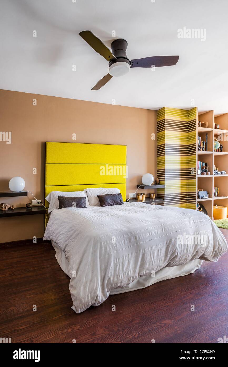 Cómoda cama con cabecero amarillo brillante en un moderno apartamento estudio decorado en un estilo minimalista Foto de stock