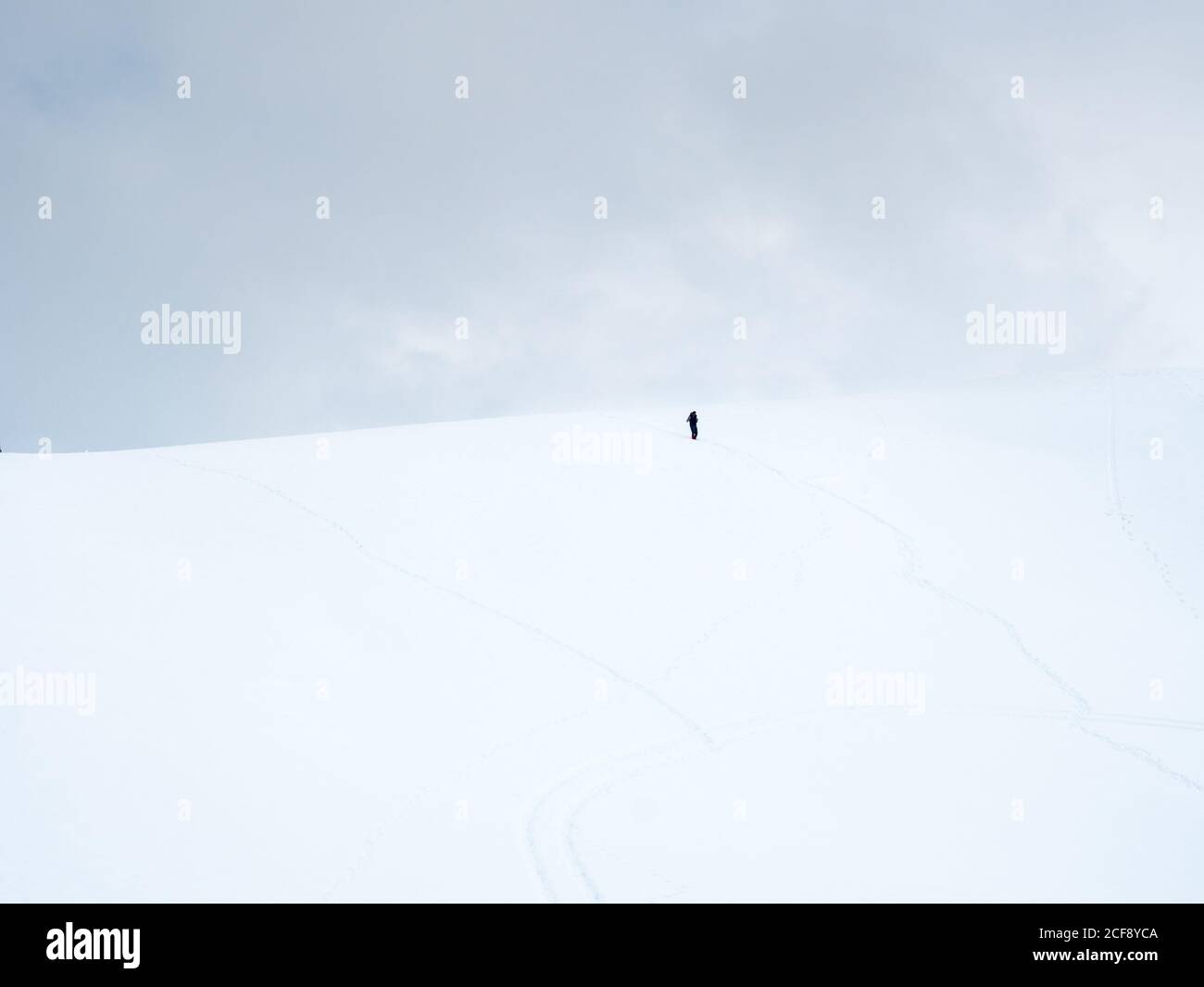 Figura oscura de persona solitaria caminando en una colina nevada día nublado Foto de stock
