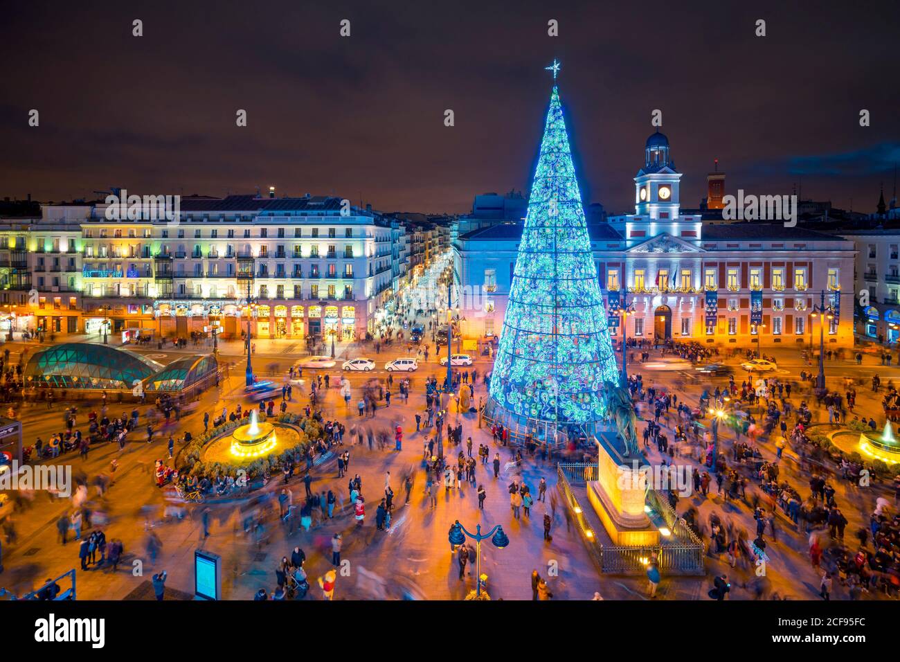 Madrid, España - 19 de diciembre de 2018: Gente disfrutando de la noche de invierno en la plaza de la ciudad Puerta del Sol con árbol de Navidad alto y luminoso decorado con luces azules y edificios iluminados Foto de stock