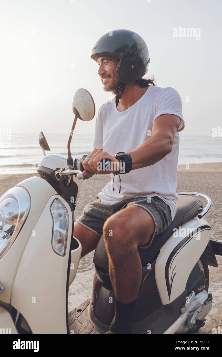 Vista lateral de un hombre feliz y activo vestido de t blanco camisa con  pantalones cortos y casco negro de moto en verano noche en la playa  Fotografía de stock - Alamy
