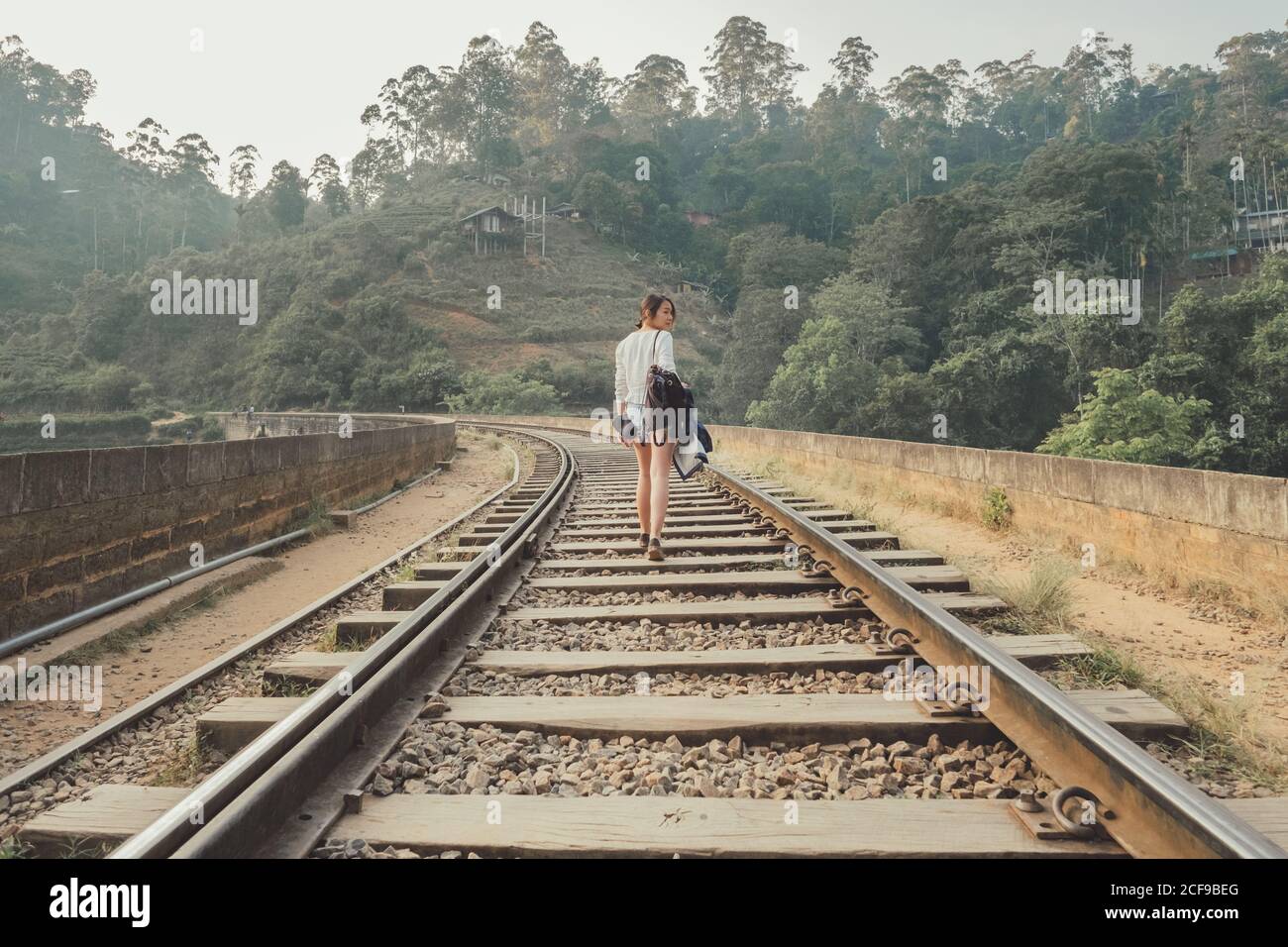 mujer anónima que camina en ferrocarril solitario contra el bosque exótico Foto de stock