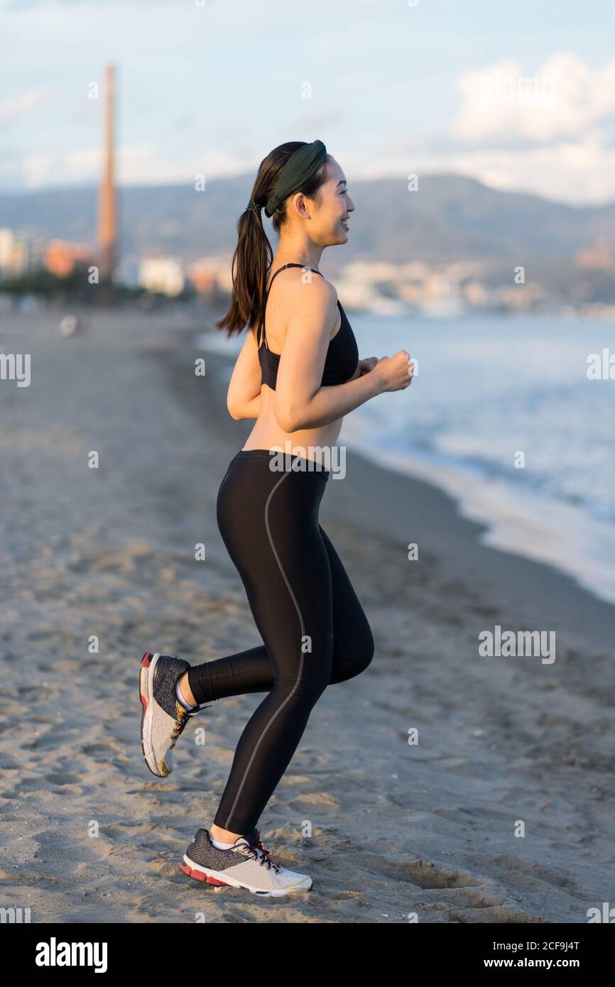 Vista lateral de la joven atleta motivada en negro activo use y zapatillas  de deporte para correr a lo largo de la costa vacía de arena Fotografía de  stock - Alamy