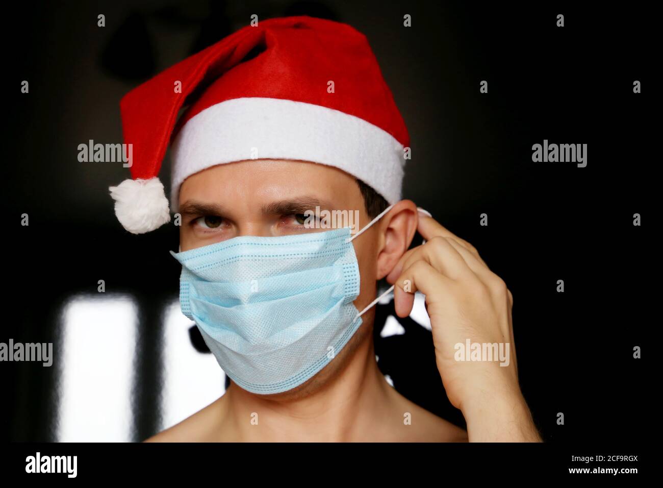 Retrato del hombre en máscara médica y sombrero de Santa Claus. Celebración navideña durante la pandemia del coronavirus Foto de stock