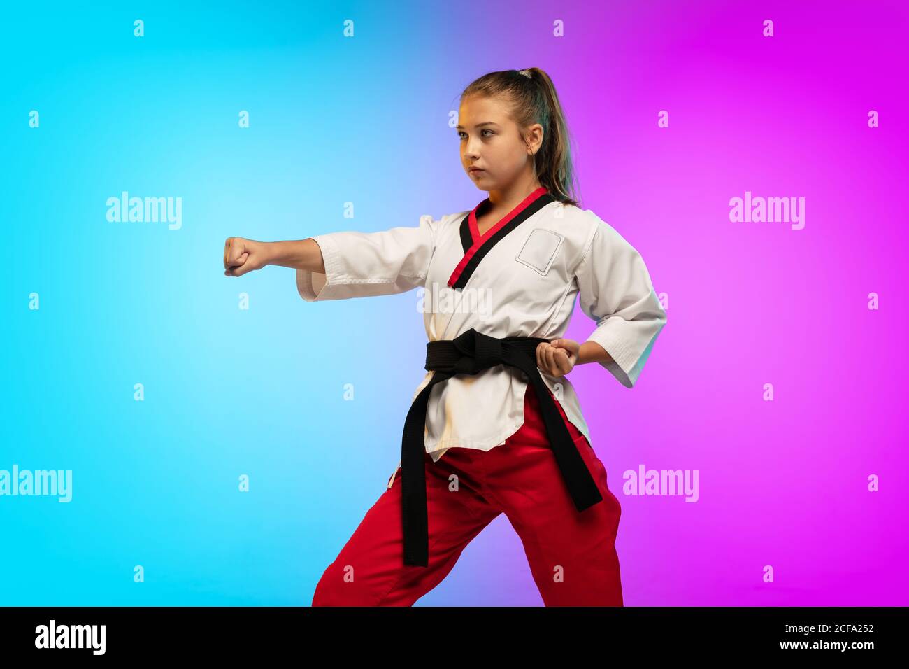 Práctica. Karate, niña taekwondo con cinturón negro aislado sobre fondo  degradado en luz de neón. Pequeño modelo caucásico, deporte de  entrenamiento infantil en movimiento y acción. Deporte, movimiento,  concepto infantil Fotografía de