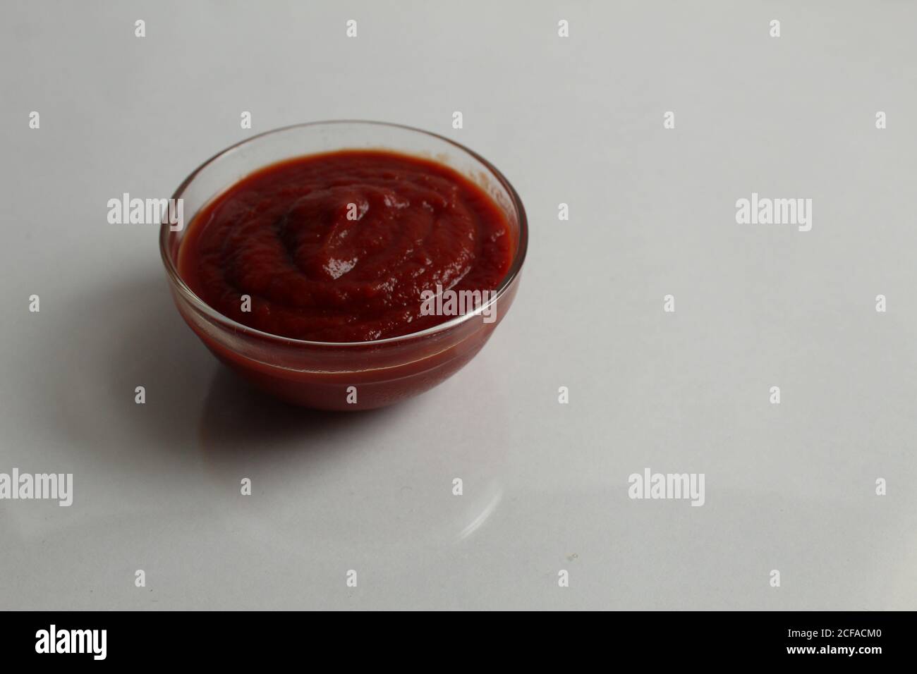 el tomate rojo caliente o la salsa dulce se vierte en un plato de cazuela de cristal sobre una copia de fondo gris blanco espacio Foto de stock
