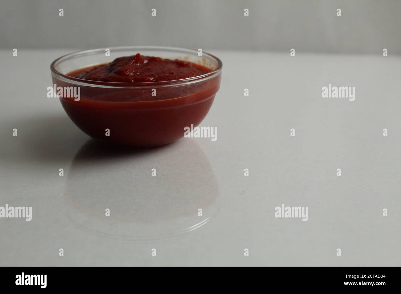 el tomate rojo caliente o la salsa dulce se vierte en un plato de cazuela de cristal sobre una copia de fondo gris blanco espacio Foto de stock