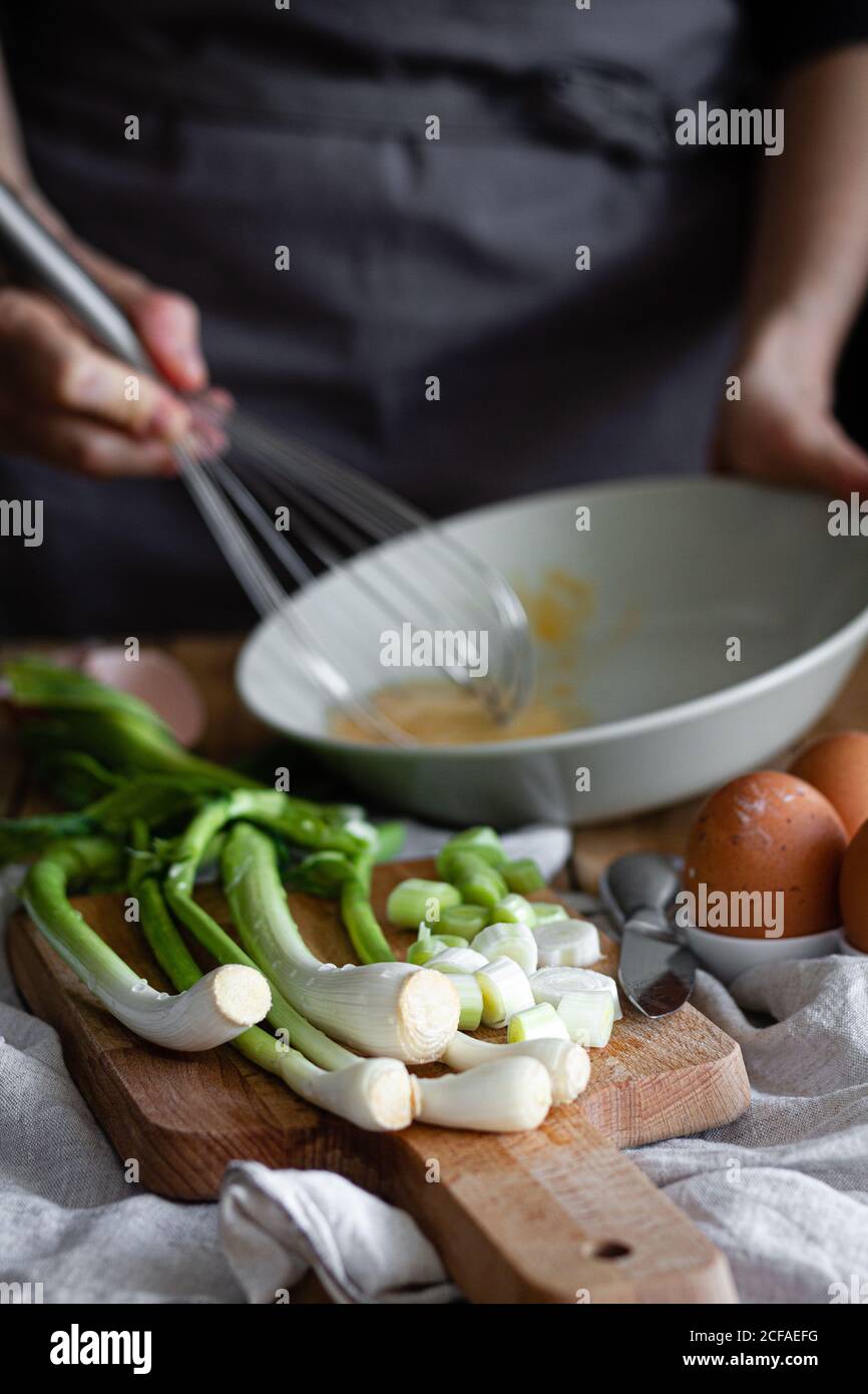 Manojo de cebolletas y champiñones frescos colocados en la tabla de corte cerca de huevos y semillas de amapola contra la mezcla de ingredientes de la ama de casa de la cosecha en el cuenco Foto de stock