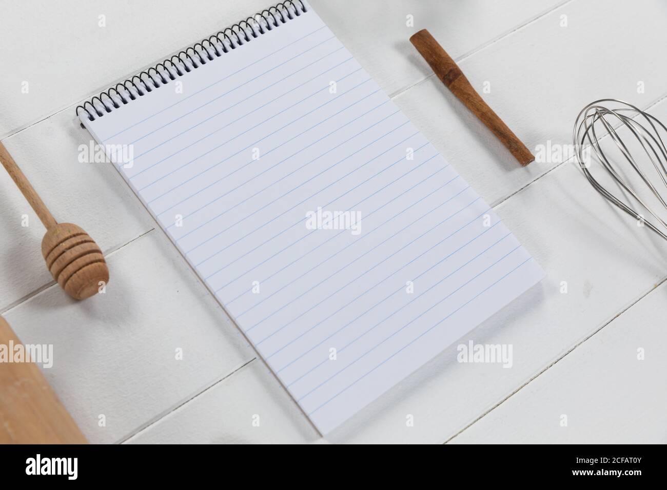 Vista de una composición con un cuaderno con cuchara de madera y susurrar sobre una superficie de madera blanca Foto de stock