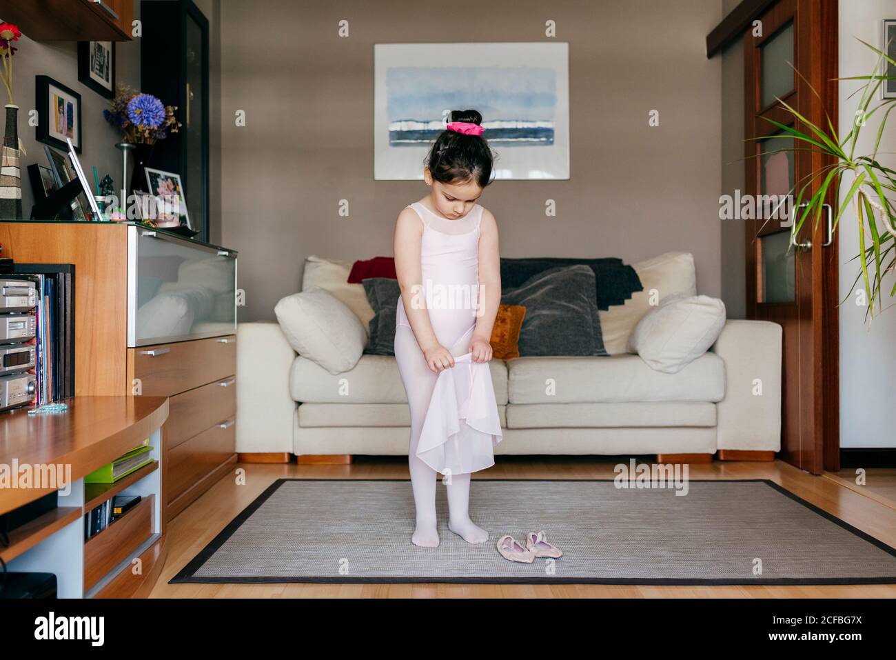 Íntimo Barcelona orgánico Linda niña en un leotardo rosa claro y medias de poner en la falda mientras  que está de pie cerca de zapatos de baile en la vida acogedora habitación  en casa Fotografía