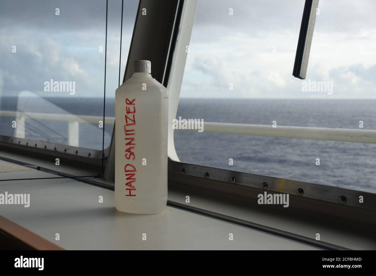 Botella de plástico con esterilizador de mano en el puente de navegación cerca de la ventana delantera del buque mercante de contenedores de carga para proteger a la tripulación y los pilotos. Foto de stock