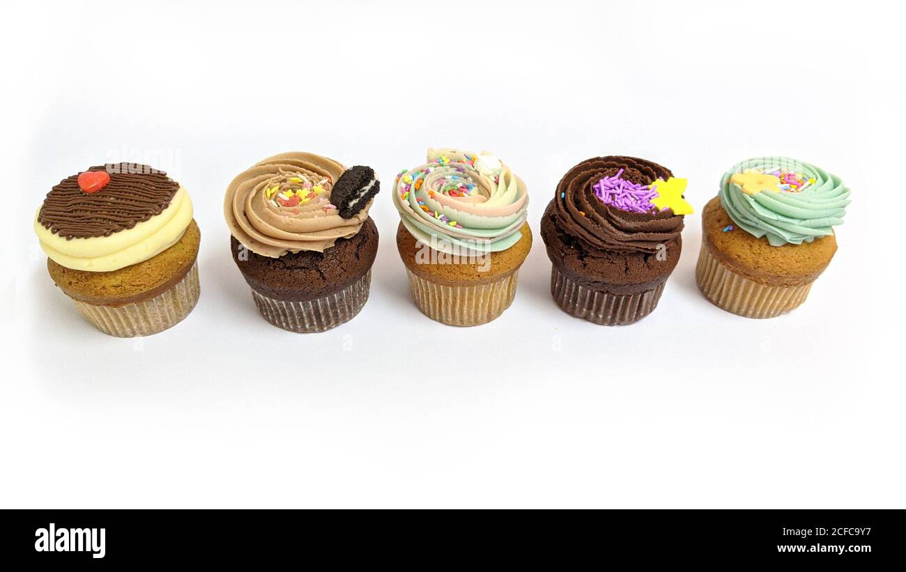 Cupcakes chocolate y vainilla deliciosos pasteles decorados en una fila sobre fondo blanco Foto de stock