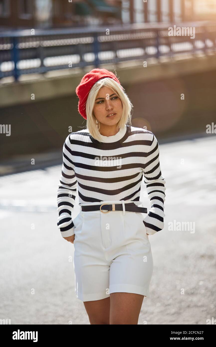 tonto temor limpiar Joven mujer rubia con camisa a rayas negras y blancas y gorra francesa roja  caminando sobre un fondo borroso de la ciudad Fotografía de stock - Alamy