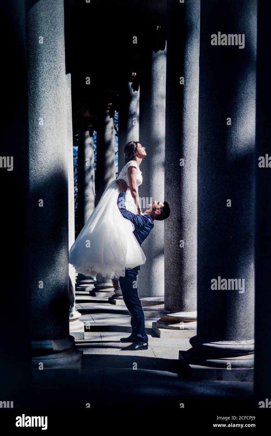 Vista lateral del joven hombre elegante sosteniendo en manos mujer en la  boda vestido entre columnas en la calle en el día soleado Fotografía de  stock - Alamy