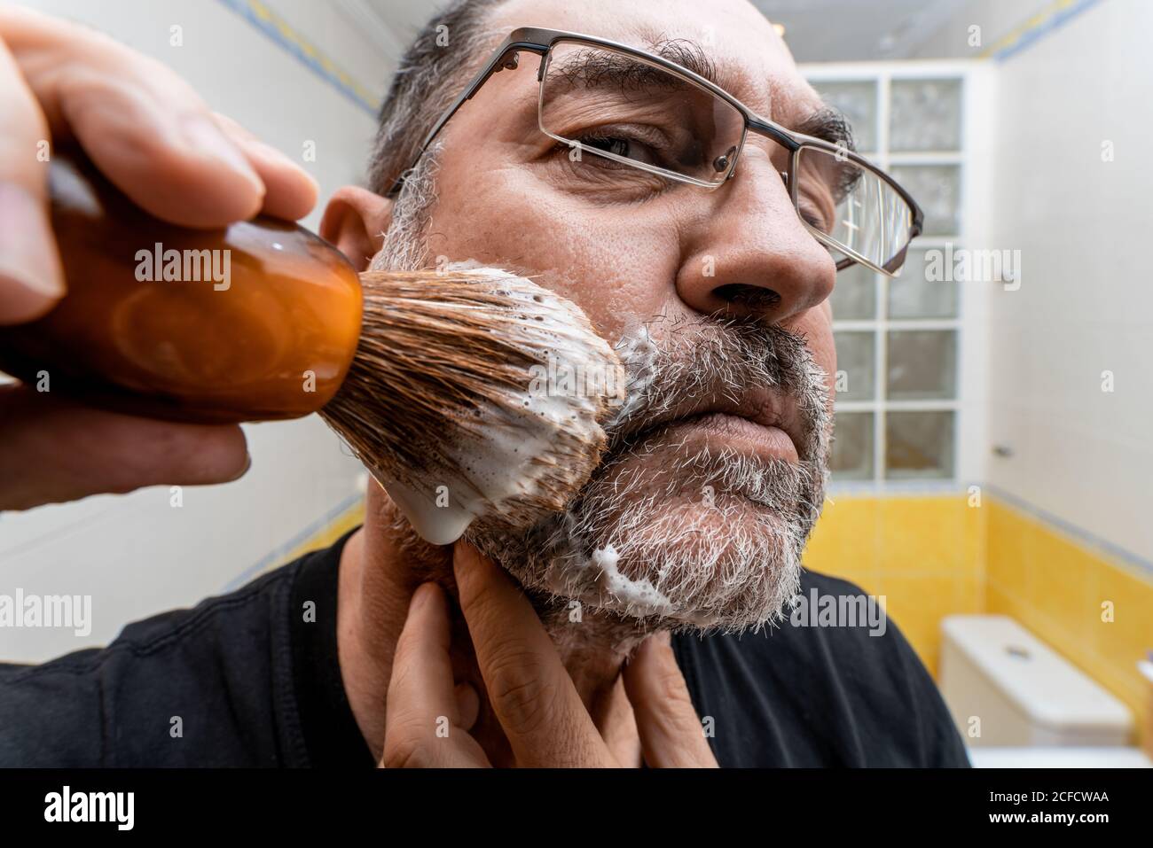 bajo ángulo cierre de macho con barba maduro aplicando espuma de afeitar  con cepillo mientras se prepara para el procedimiento de afeitado en el  baño Fotografía de stock - Alamy