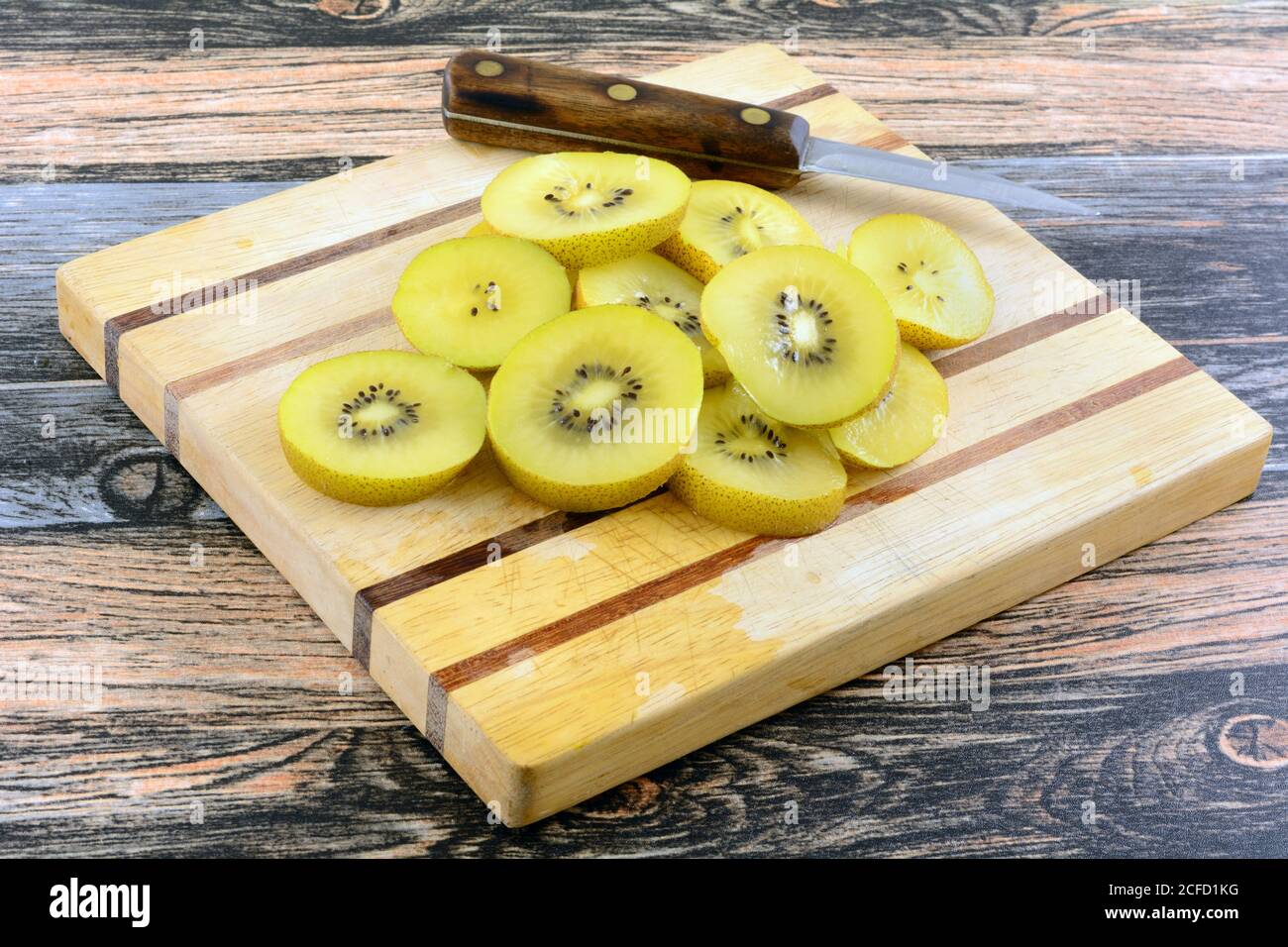 Rodajas de kiwi amarillo dorado sobre tabla de madera con cocina cuchillo Foto de stock