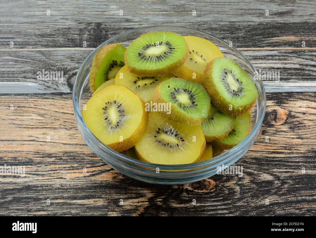 Rebanadas de fruta de kiwi verde y amarillo dorado frescas crudas cuenco de cristal en la mesa Foto de stock