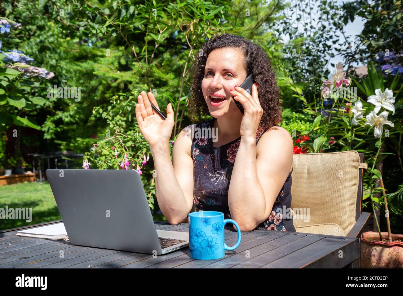 Mujer joven caucásica trabajando en un ordenador portátil desde casa en un jardín. Foto de stock