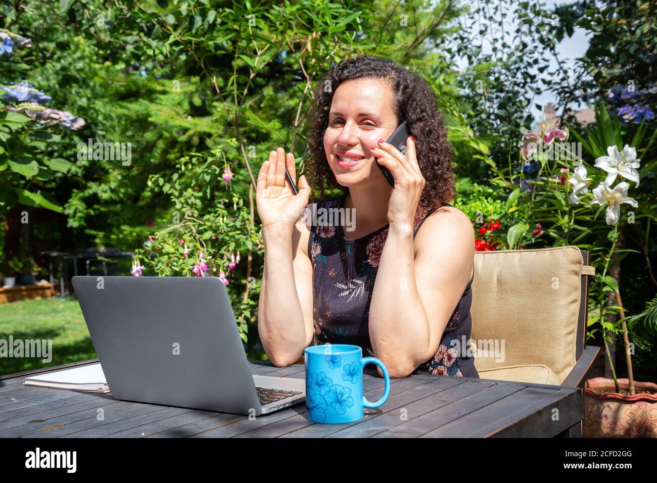 Mujer joven caucásica trabajando en un ordenador portátil desde casa en un jardín. Foto de stock