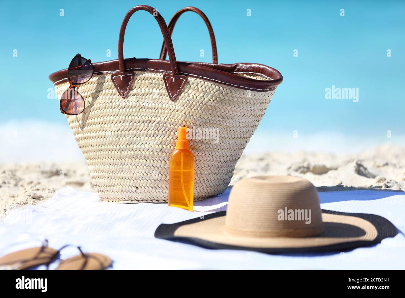 Accesorios de playa para mujer en la arena para el concepto de vacaciones  de verano. Bolsa de paja, sombrero y crema solar o bronceado botella de  aerosol de aceite con Fotografía de