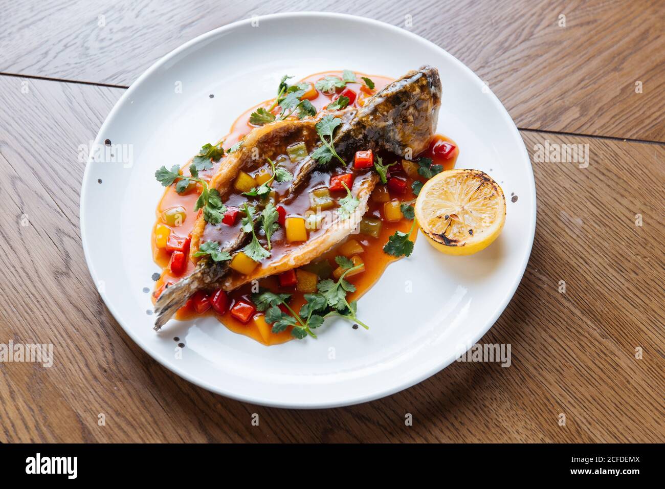 Desde arriba de todo el pescado blanco asado cortado y relleno con salsa de tomate y verduras adornadas con cilantro verde Foto de stock
