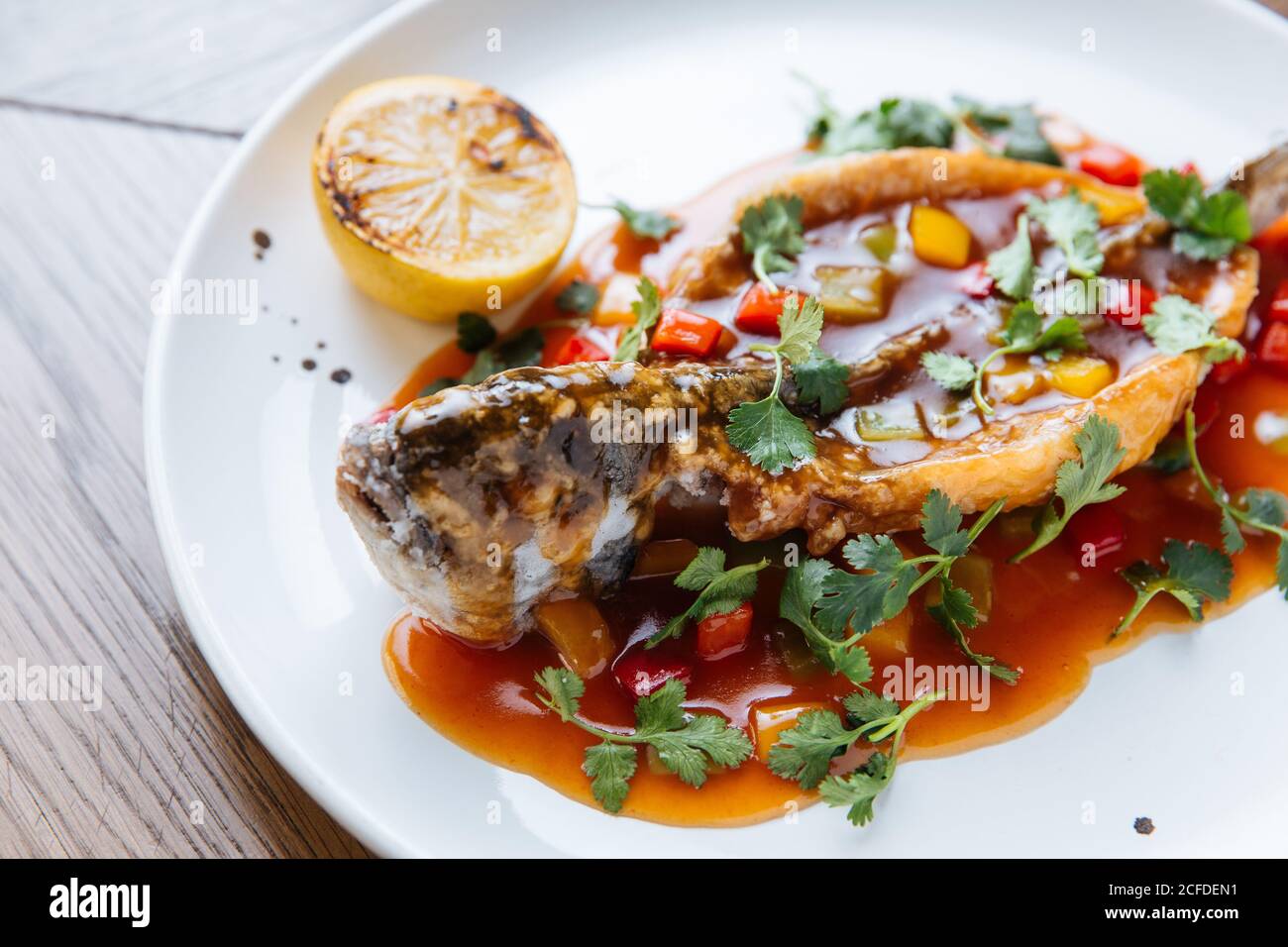 Desde arriba de todo el pescado blanco asado cortado y relleno con salsa de tomate y verduras adornadas con cilantro verde Foto de stock