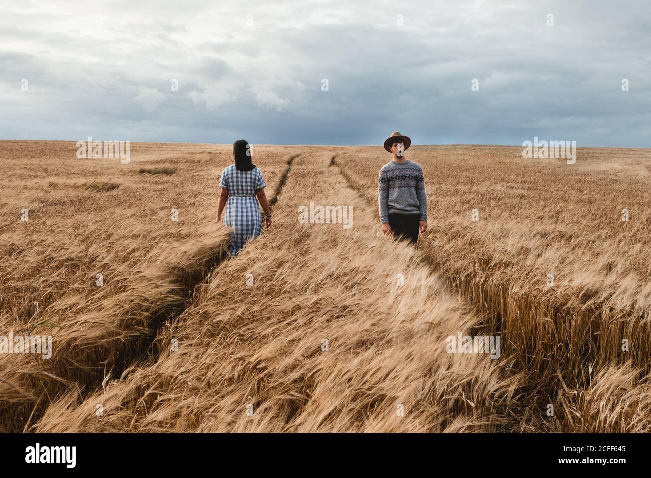 Mujer en vestido de cuadros y hombre en suéter y sombrero caminar en  direcciones opuestas en senderos paralelos entre boundless marrón Campo  escocés con cielo nublado en el fondo Fotografía de stock -