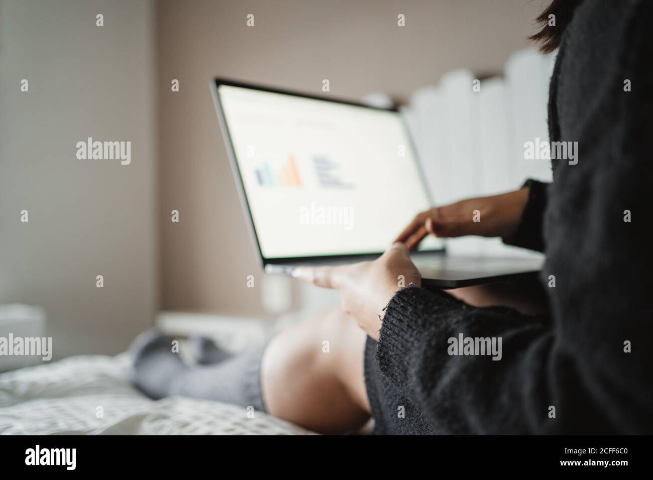 Recorte a una mujer joven escribiendo en el ordenador portátil mientras estudia y se acuesta en la cama en casa en París Foto de stock