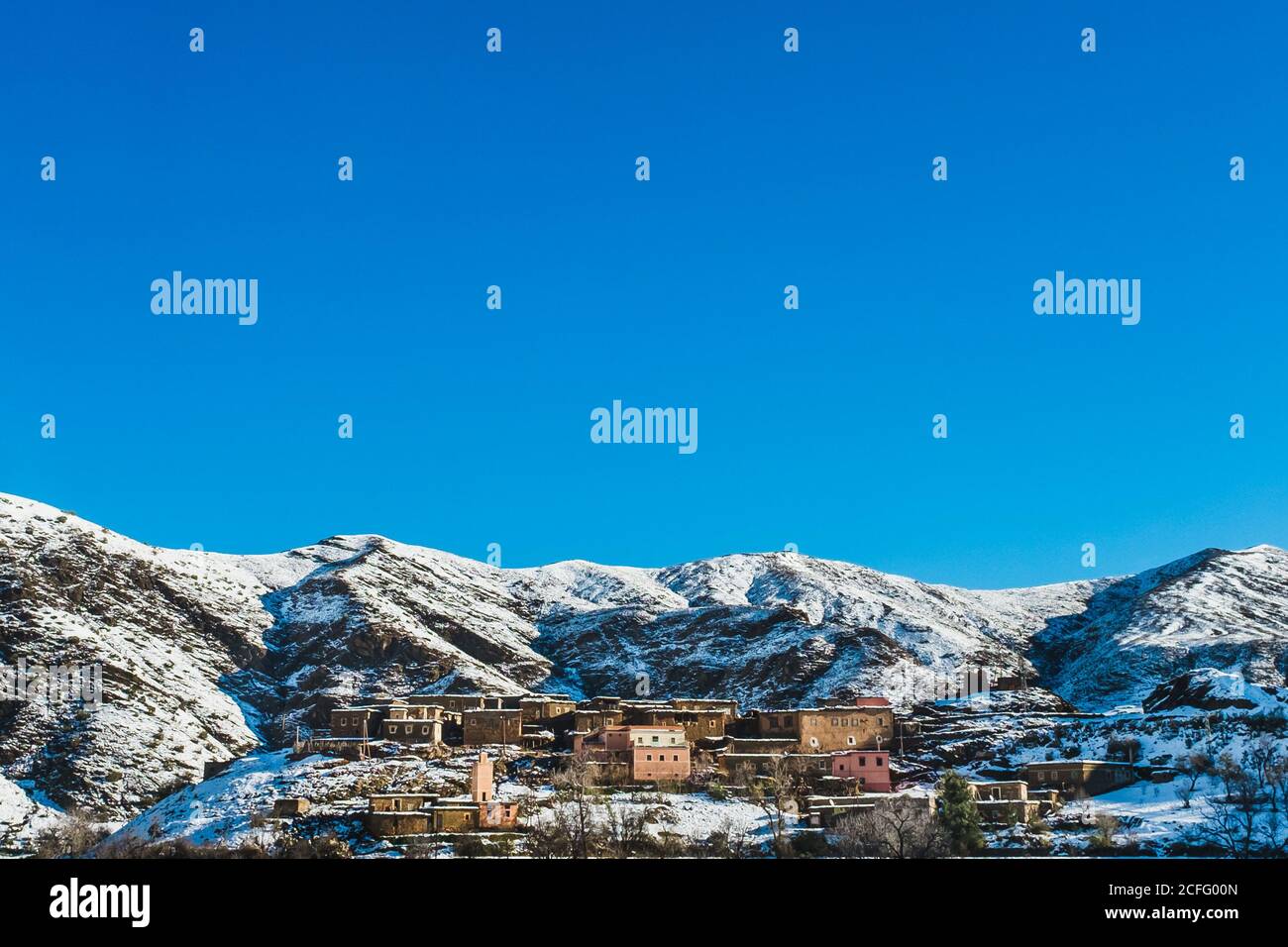 Bajo ángulo de casas residenciales situadas en la ladera de la montaña cresta cubierta de nieve sobre fondo de cielo azul sin nubes Foto de stock