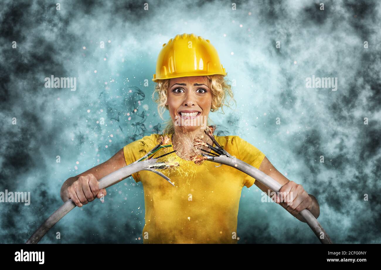 Una chica trabajadora con sombrero rompe un cable eléctrico. Fondo cian Foto de stock