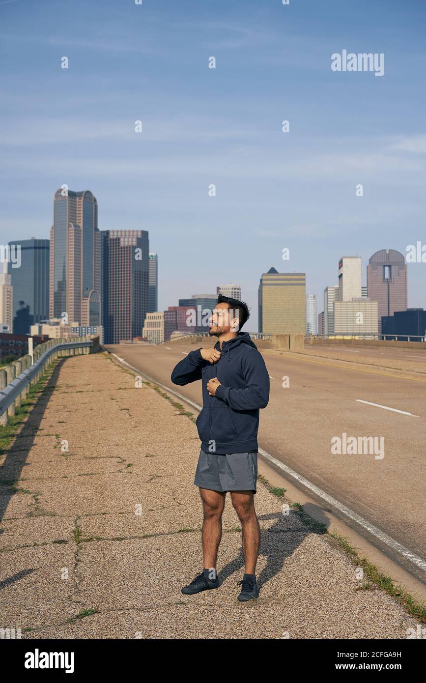 Joven atleta hispano masculino en ropa deportiva con los ojos cerrados después del entrenamiento de pie en el lado de la carretera en el centro de Dallas, Texas Foto de stock
